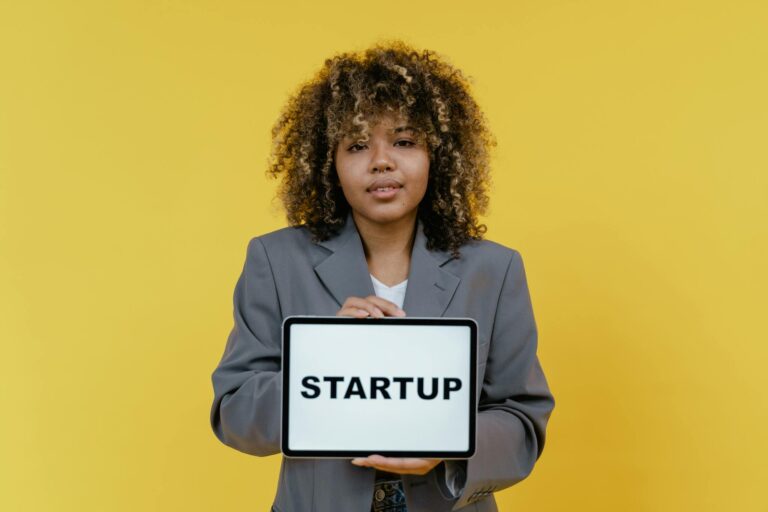 Portrait of a woman holding a tablet showing the word 'STARTUP' against a yellow background.